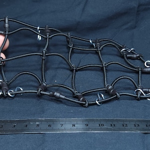 May include: Black cargo net with hooks, measuring 38 cm in length. The net is made of elastic material and has a grid pattern.