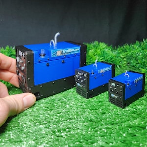 以下が含まれることがあります： 異なるサイズの3つの青と黒のTrailblazer溶接機。最大の溶接機には「Trailblazer」と書かれたラベルが付いています。