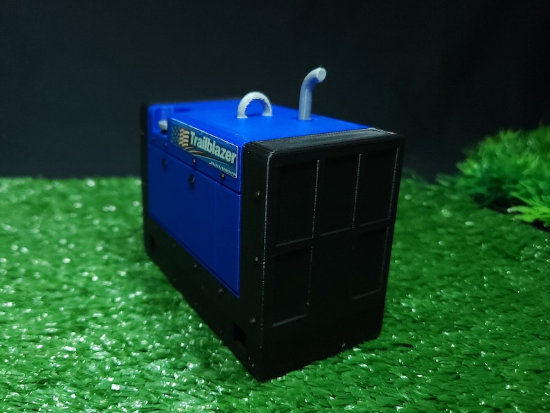 以下が含まれることがあります： グレーの排気管が付いた青と黒のトレイルブレイザー発電機。発電機は緑の人工芝の上に置かれています。