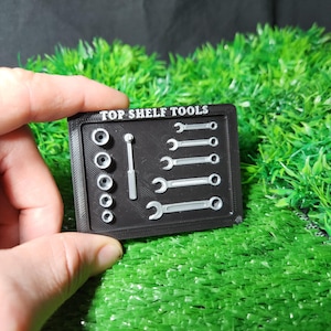 Puede incluir: Un organizador de herramientas de plástico negro con el texto "TOP SHELF TOOLS" impreso en la parte delantera. El organizador contiene una variedad de herramientas, incluyendo llaves y enchufes.