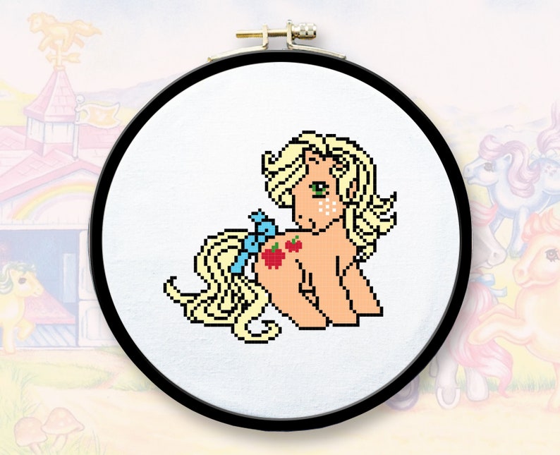 Peut inclure: Un cerceau de broderie en point de croix avec une image pix&eacute;lis&eacute;e d'un poney brun clair avec une crini&egrave;re et une queue blondes. Le poney a un n&oelig;ud bleu et trois pommes rouges sur son flanc.