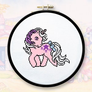 May include: A pink and purple My Little Pony with a blue bow and a star-shaped cutie mark. The pony is embroidered on a white fabric in a round embroidery hoop.
