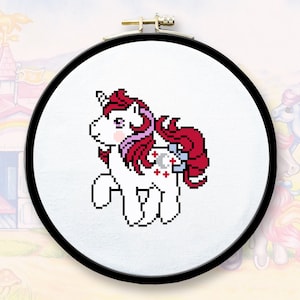 May include: A white unicorn with a red and pink mane and tail. The unicorn has a blue and silver star symbol on its flank. The unicorn is embroidered on a white fabric in a round embroidery hoop.