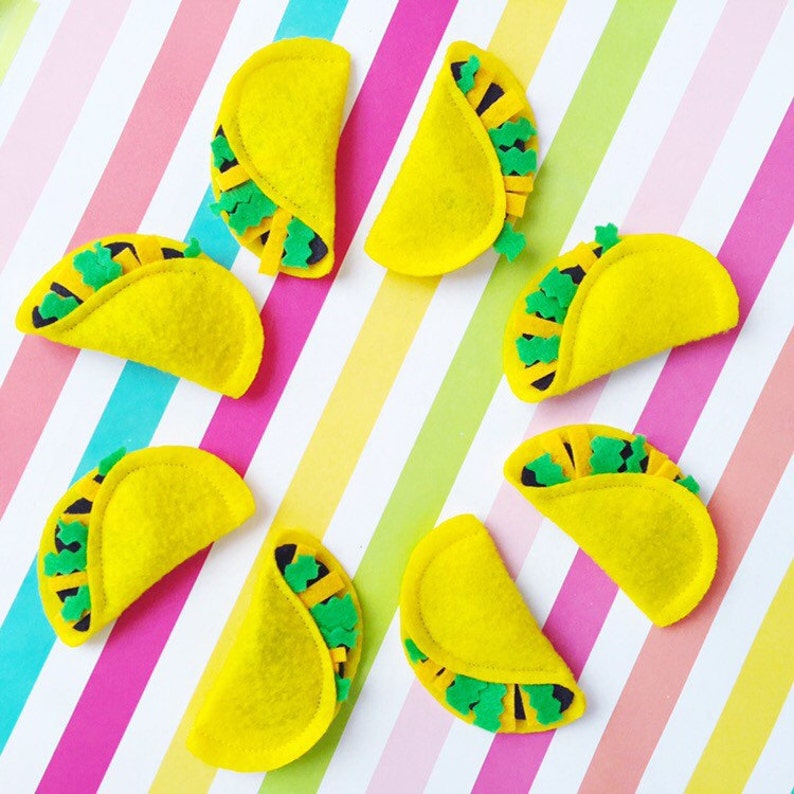 May include: Eight yellow felt tacos with green felt fillings. The tacos are arranged in a circle on a striped background.