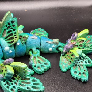 Puede incluir: Un juguete articulado verde y azul con un dise&ntilde;o de mariposa. El juguete est&aacute; hecho de pl&aacute;stico y tiene un cuerpo segmentado con m&uacute;ltiples alas.