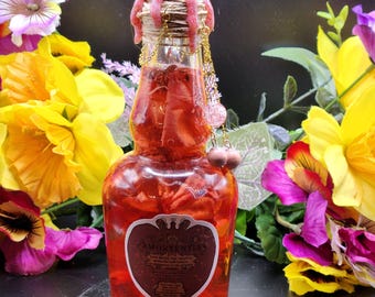 May include: A clear glass bottle filled with red liquid and submerged red petals, featuring a label that reads Amortentia. The bottle neck is wrapped in twine and topped with pink wax, adorned with gold chains and small pink spherical beads.