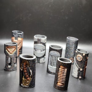 May include: A collection of cylindrical, steampunk-style objects with metallic accents. The designs feature copper, silver, and bronze elements, with intricate details and a textured finish. The objects are arranged against a dark background.