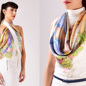 May include: A silk scarf with a colourful design, worn as a halter top and around the neck. The scarf features a white background with a pattern of leaves, feathers, and other abstract shapes in shades of yellow, purple, and blue.