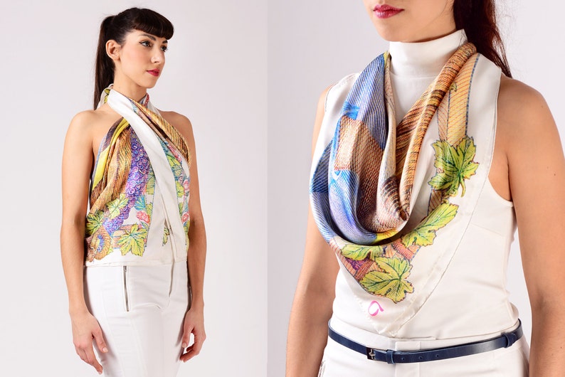 May include: A silk scarf with a colourful design, worn as a halter top and around the neck. The scarf features a white background with a pattern of leaves, feathers, and other abstract shapes in shades of yellow, purple, and blue.