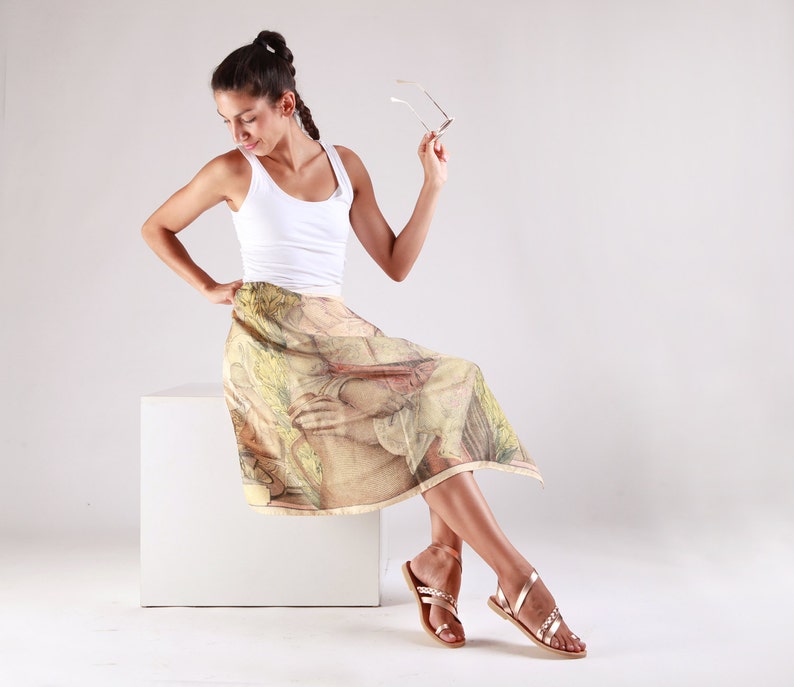 May include: A woman wearing a white vest top and a printed skirt sits on a white platform. She is holding a pair of sunglasses in her right hand.