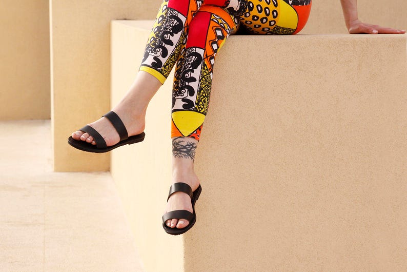 Puede incluir: Una persona con sandalias negras y leggings con estampado colorido. Los leggings tienen un dise&ntilde;o geom&eacute;trico con colores amarillo, naranja, rojo y negro.