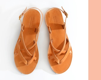 May include: A pair of tan leather sandals with criss-cross straps and a buckle closure. The sandals have the text "SAVOPOLIOS" on the straps.