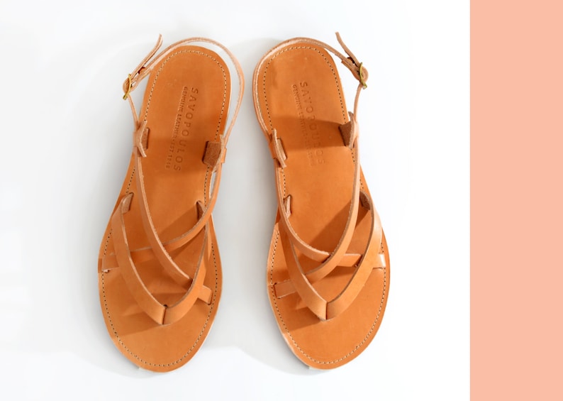 May include: A pair of tan leather sandals with criss-cross straps and a buckle closure. The sandals have the text "SAVOPOLIOS" on the straps.