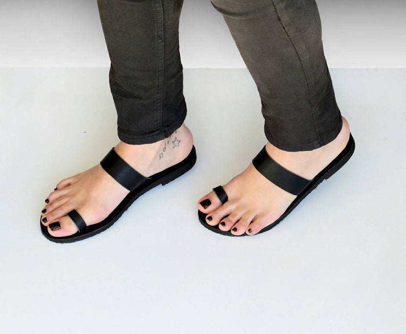 Peut inclure: Sandales &agrave; lani&egrave;res en cuir noir avec un anneau de toe. Les sandales sont plates et ont un design simple.