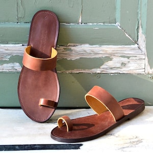 Peut inclure: Une paire de sandales en cuir marron avec une boucle d'orteil et une seule sangle sur le pied. Les sandales ont une doublure en cuir marron clair.