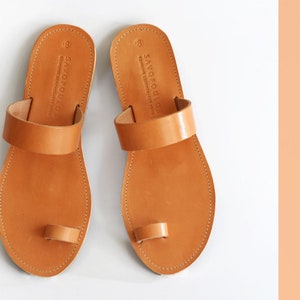 Peut inclure: Une paire de sandales en cuir marron avec une boucle d'orteil et une seule sangle sur le pied. Les sandales sont fabriqu&eacute;es par Savopoulos, une marque connue pour ses articles en cuir de haute qualit&eacute;.