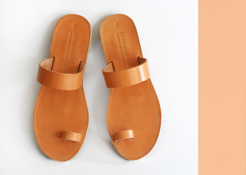 Peut inclure: Une paire de sandales en cuir marron avec une boucle d'orteil et une seule sangle sur le pied. Les sandales sont fabriqu&eacute;es par Savopoulos, une marque connue pour ses articles en cuir de haute qualit&eacute;.