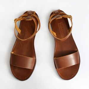 May include: A pair of brown leather sandals with adjustable ankle straps. The straps are made of a lighter brown leather and have a buckle closure.