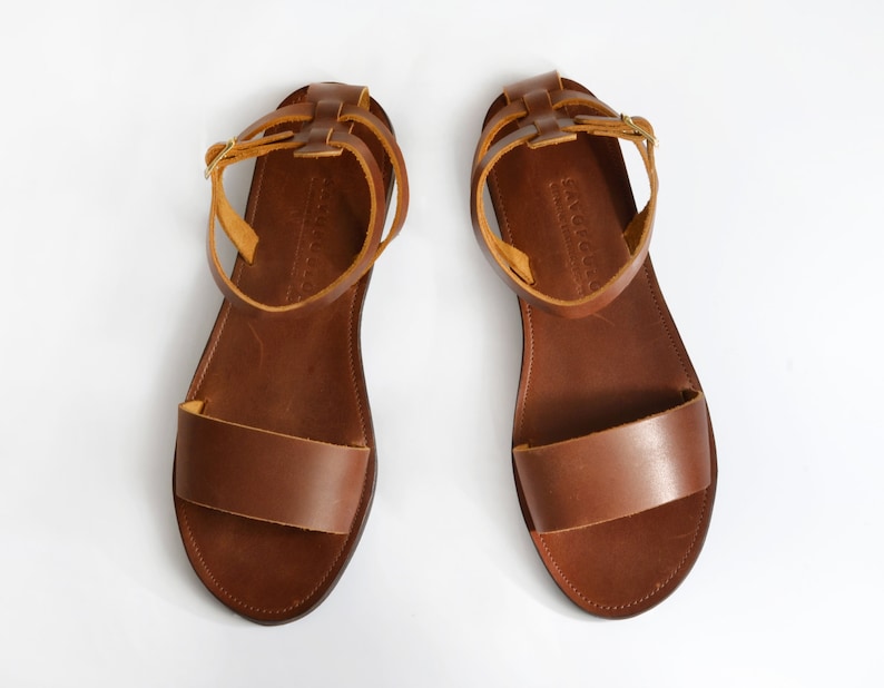 May include: A pair of brown leather sandals with adjustable ankle straps. The straps are made of a lighter brown leather and have a buckle closure.