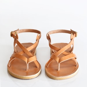 May include: A pair of tan leather sandals with criss-cross straps and a buckle closure.