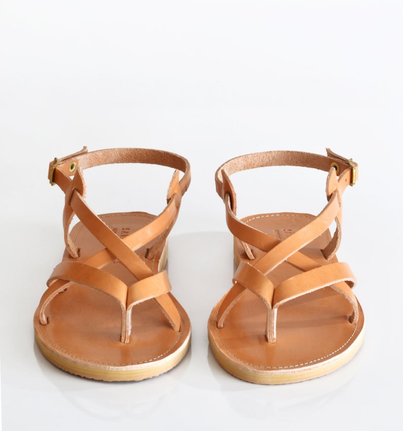 May include: A pair of tan leather sandals with criss-cross straps and a buckle closure.