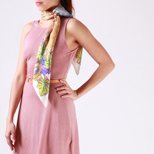 May include: A sleeveless, dusky pink dress with a matching belt. A colourful silk scarf with a leaf and grape design is draped around the neck. The scarf features shades of green, purple, and yellow.