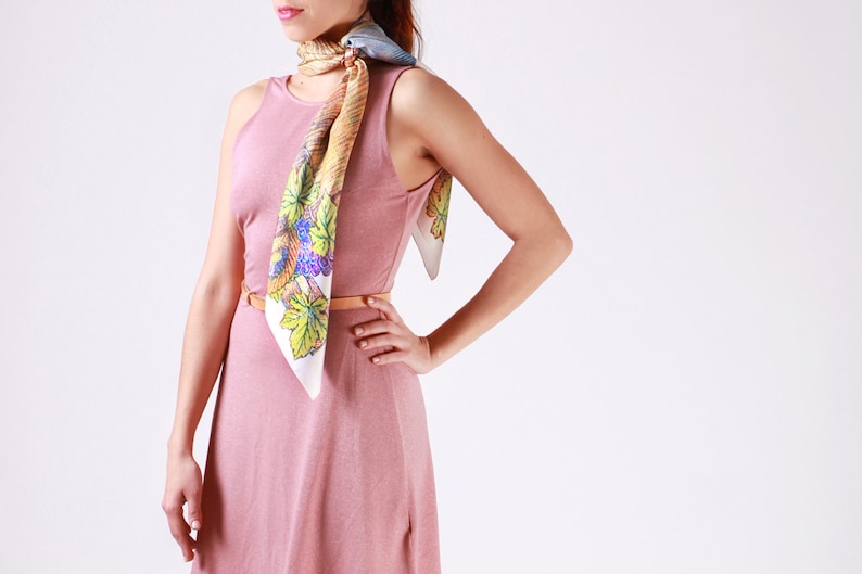 May include: A sleeveless, dusky pink dress with a matching belt. A colourful silk scarf with a leaf and grape design is draped around the neck. The scarf features shades of green, purple, and yellow.