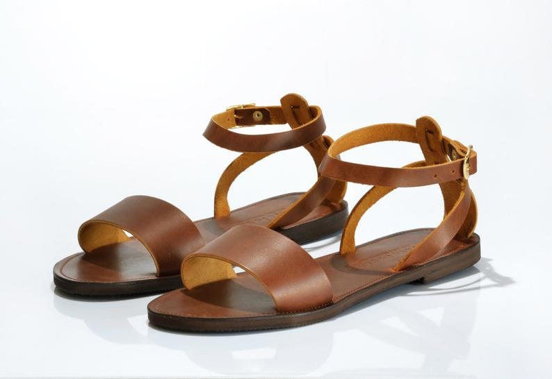 May include: A pair of brown leather sandals with ankle straps and buckles. The sandals have a flat sole and a simple design.