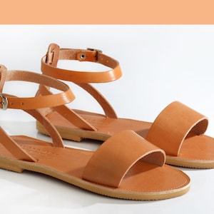 May include: Two pairs of brown leather sandals with ankle straps and buckles. The sandals have a flat sole and a simple design.
