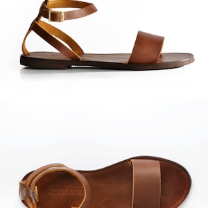 May include: Brown leather sandals with a single strap across the foot and an ankle strap with a gold buckle. The sandals have a flat sole.
