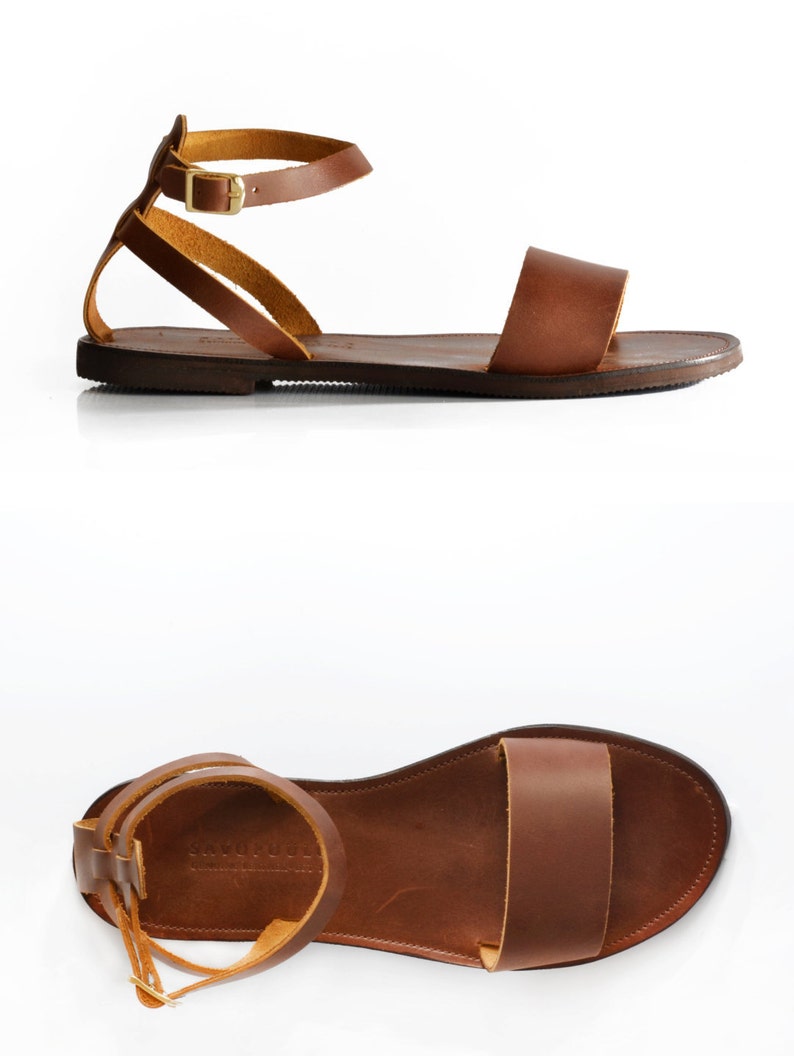 May include: Brown leather sandals with a single strap across the foot and an ankle strap with a gold buckle. The sandals have a flat sole.