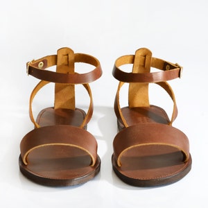 May include: A pair of brown leather sandals with ankle straps. The sandals have a simple design and are made of high-quality leather.