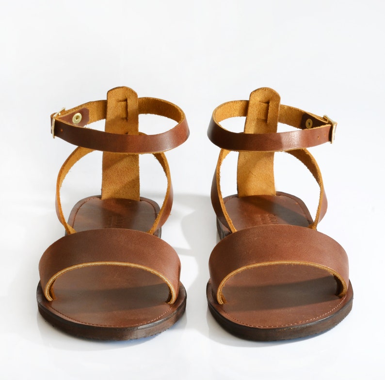 May include: A pair of brown leather sandals with ankle straps. The sandals have a simple design and are made of high-quality leather.