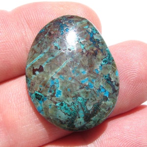 May include: A smooth, oval-shaped cabochon of chrysocolla with a mottled pattern of blue, green, and brown. The stone is polished and has a glossy finish.
