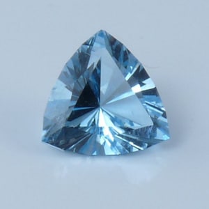 May include: A triangular, faceted gemstone with a light blue color. The gemstone is cut in a triangular shape and has a high degree of brilliance.