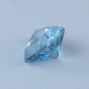 May include: A light blue gemstone with a faceted cut. The gemstone is a square shape with pointed corners.