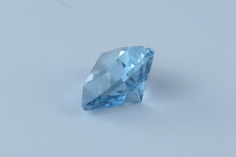 May include: A light blue gemstone with a faceted cut. The gemstone is a square shape with pointed corners.