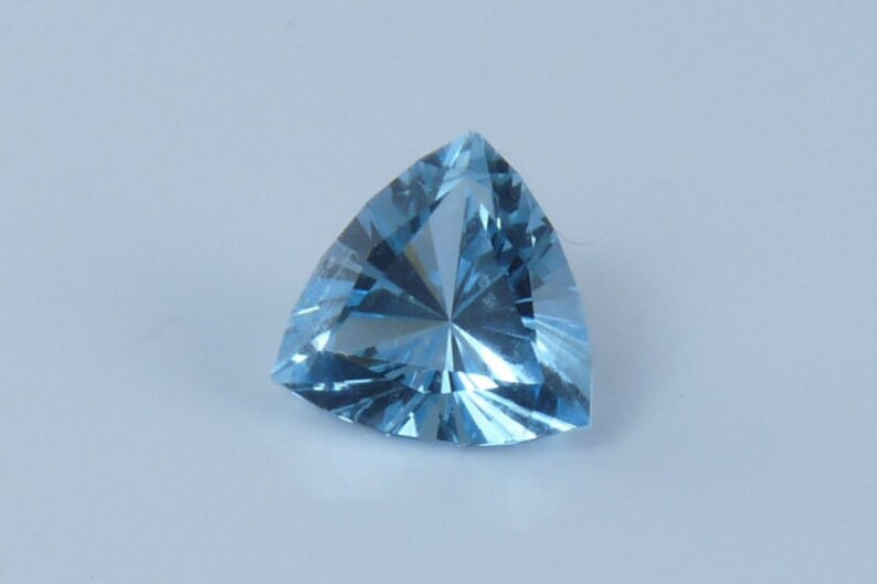 May include: A triangular, light blue gemstone with a faceted cut.