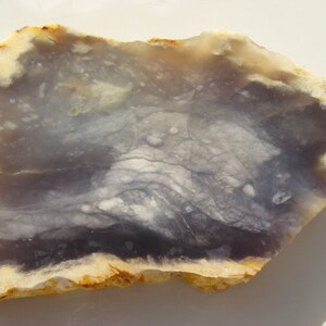 May include: A slab of purple agate with white and brown markings. The agate has a rough, natural edge.