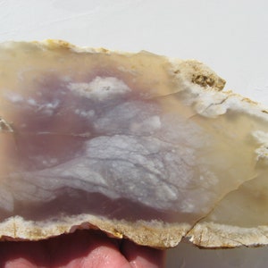 May include: A slab of agate with a white and light purple pattern. The agate has a rough, natural edge.