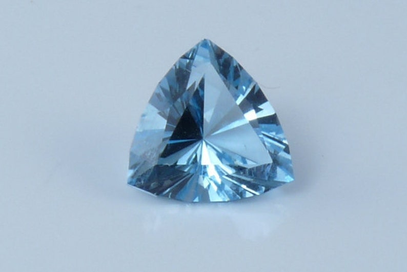 May include: A triangular, faceted gemstone with a light blue color. The gemstone is cut in a triangular shape and has a high degree of brilliance.