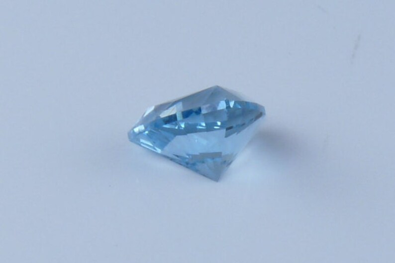 May include: A light blue gemstone with a faceted cut. The gemstone is on a white background.