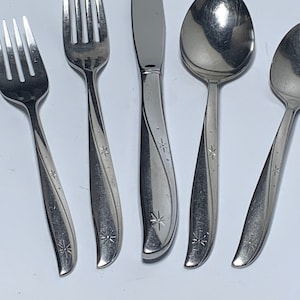 Op de afbeelding: Set van vijf zilverkleurige bestekdelen met een stervormig ontwerp op de handvatten. De set bevat een mes, twee vorken en twee lepels.