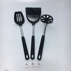 Puede incluir: Tres utensilios de cocina negros con mangos plateados. Los utensilios son una cuchara ranurada, una espátula ranurada y un machacador de patatas. Los utensilios están etiquetados como A, B y D.