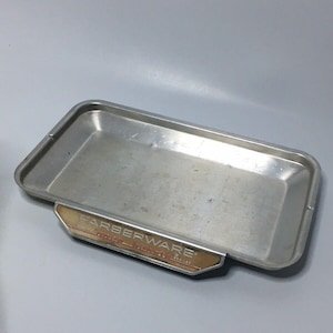 May include: A silver baking sheet with a gold label that reads "Farberware Aluminum Cookie Sheet".