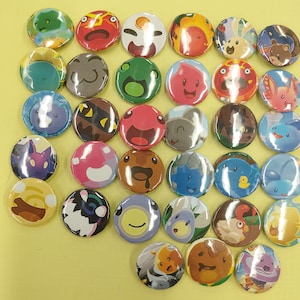 May include: A collection of colorful, round button pins with various cartoon character designs. The pins feature a variety of colors, including green, red, blue, and yellow, and are arranged on a yellow surface. Each pin has a unique, detailed illustration.