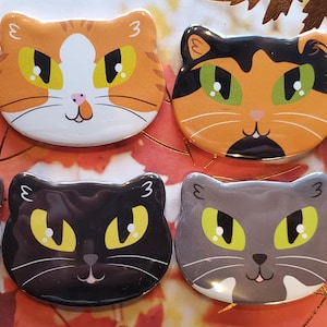 May include: Set of ten 3-inch round cat-themed pinback buttons. The buttons feature various cat breeds with different colored fur and eye colors. The buttons are all black and white with a white outline around each button.