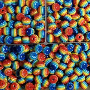 Puede incluir: Primer plano de una colección de cuentas a rayas de colores del arcoíris. Las cuentas son rojas, naranjas, amarillas, verdes y azules. Cada cuenta redonda tiene un agujero en el centro, ideal para manualidades.