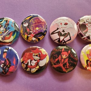 以下が含まれることがあります： アニメシリーズ「ヘルバボス」の様々なカートゥーンキャラクターが描かれた、丸いボタンが8つあります。キャラクターは、アラストア、エンジェルダスト、チャーリー、ヴァギー、サーペンティウス、ルーナ、フィザロリーです。ボタンはカラフルで、様々な表情とポーズをしています。