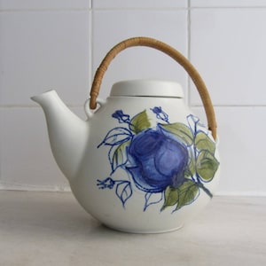 Peut inclure: Théière en céramique blanche avec un motif floral bleu et vert et une poignée en bois brun.